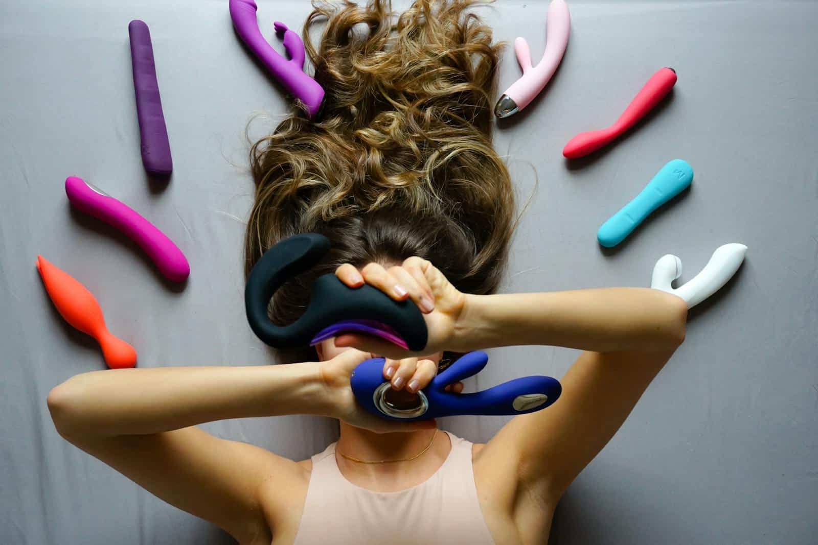 Woman Lying on the Floor and Holding a Variety of Different Vibrators