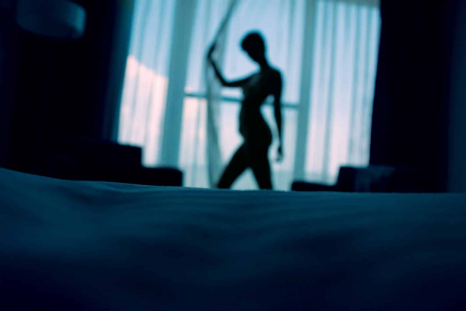 sillouehtte photo of woman standing beside window curtains